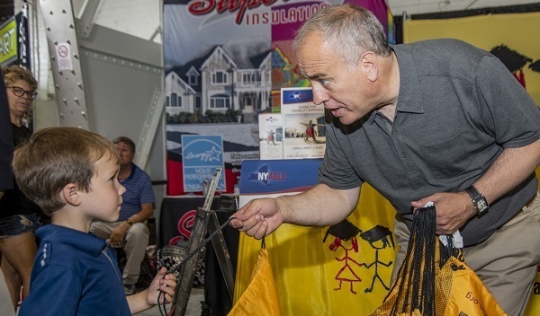 State Comptroller DiNapoli handing a 529 giveaway backpack to a child at the New York State Fair 