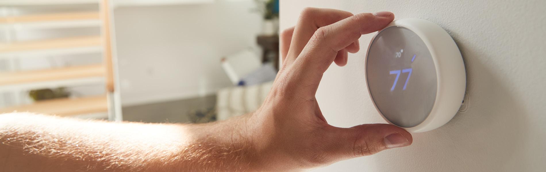 A hand turning down a thermostat.